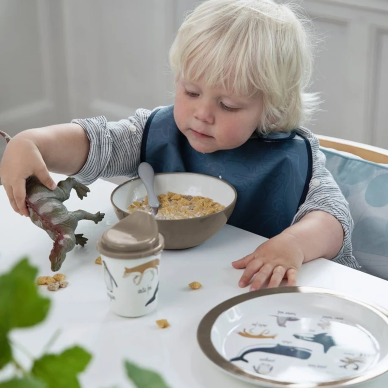 Bambino al tavolo mentre mangia e gioca con un pupazzo dinosauro