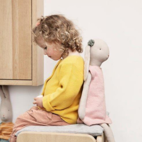 Bambina seduta con alle spalle una coniglietta di stoffa Maileg