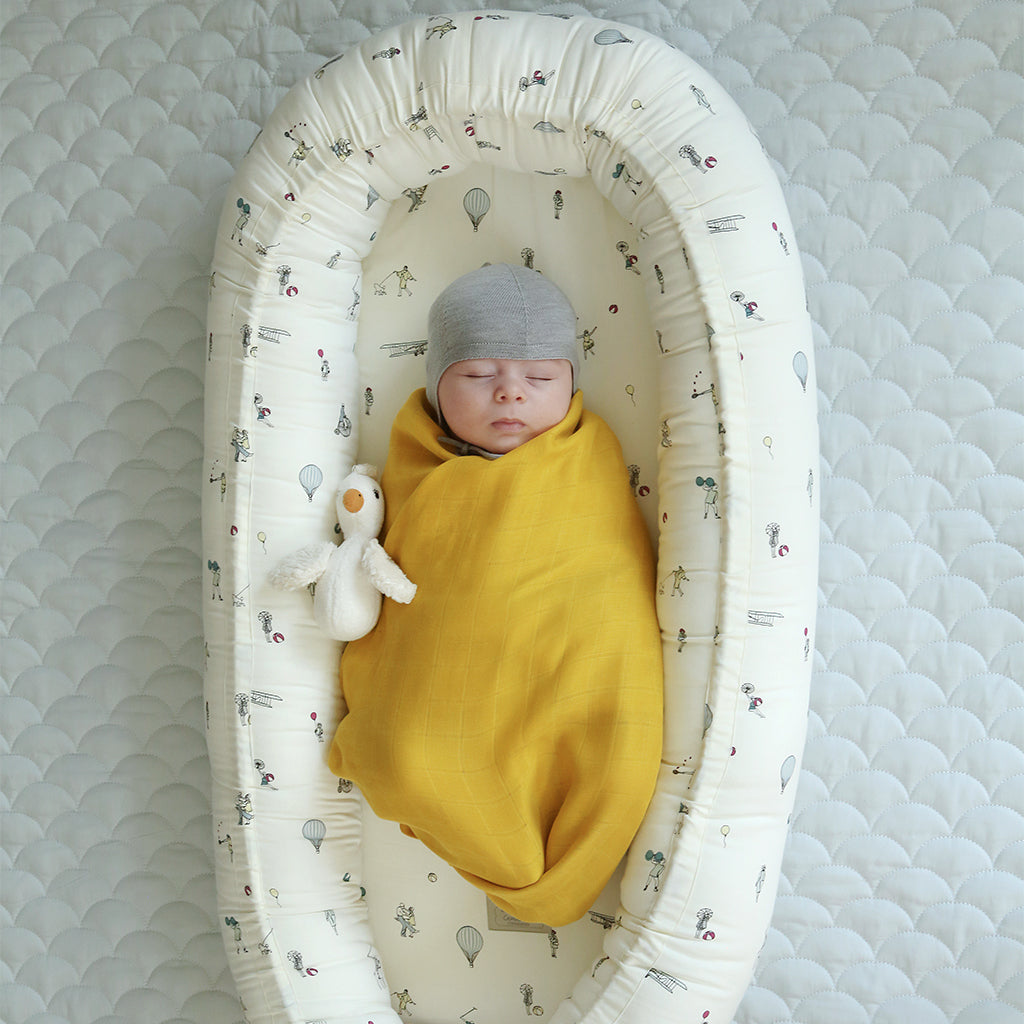 Sonaglio peluche in cotone a forma di uccellino con becco giallo accanto ad un neonato avvolto in una copertina color miee