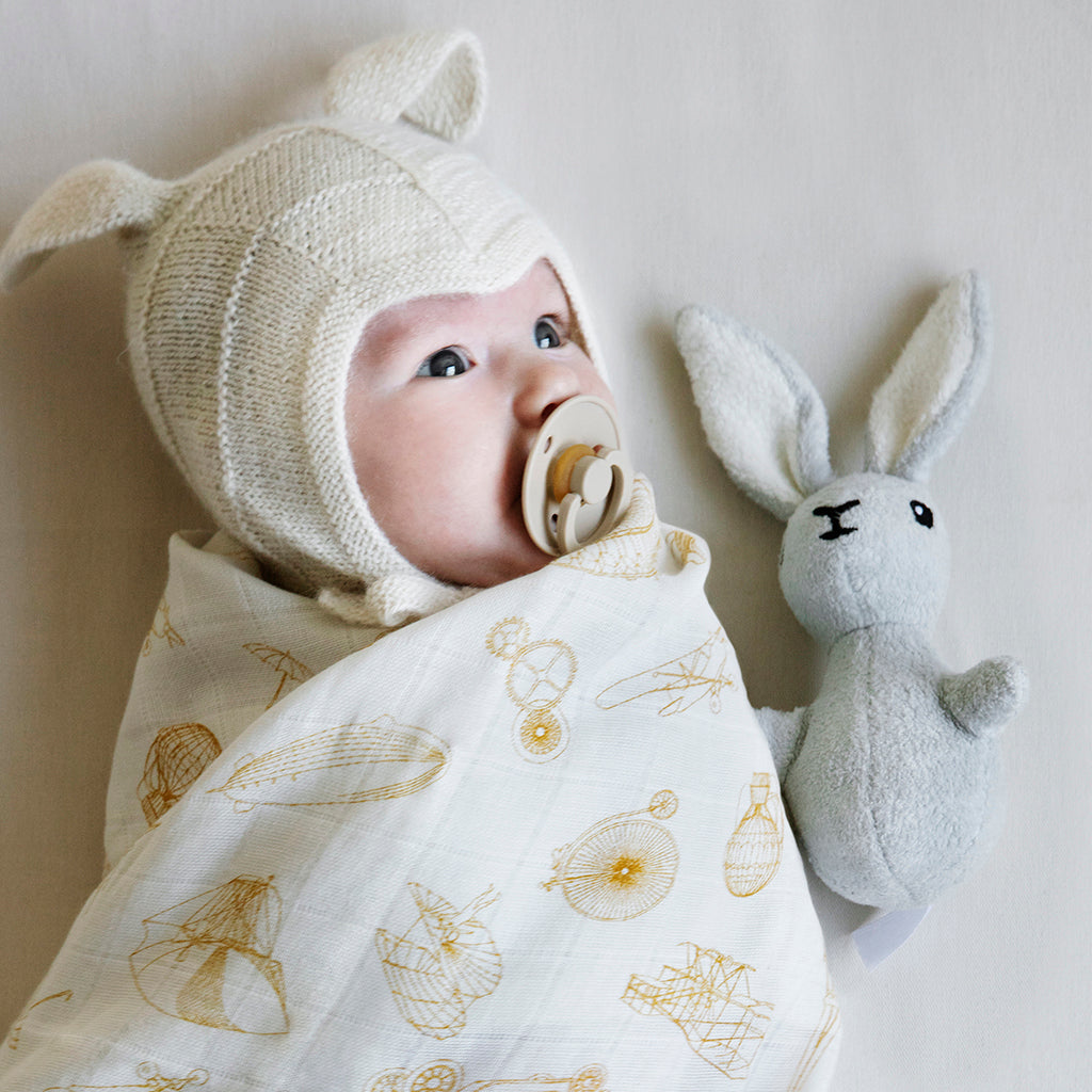 Sonaglio in stoffa a forma di leprotto accanto ad un neonato con cuffia avvolto in una copertina