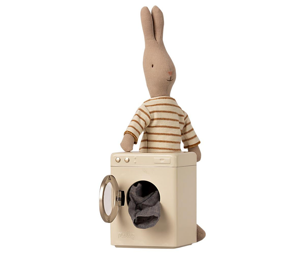 Mini lavatrice giocattolo in metallo con oblo aperto con dentro abiti e a fianco un coniglietto peluche