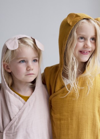 Bambina con indosso accappatoio color malva con cappuccio accanto ad una bambina con accappatoio ocra