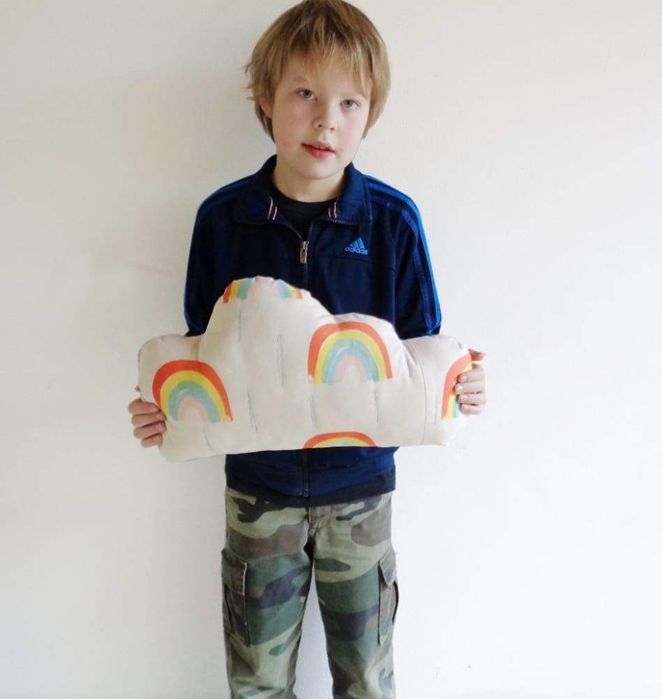 Bambino che mostra un cuscino a forma di nuvola con arcobaleno serigrafato a mano