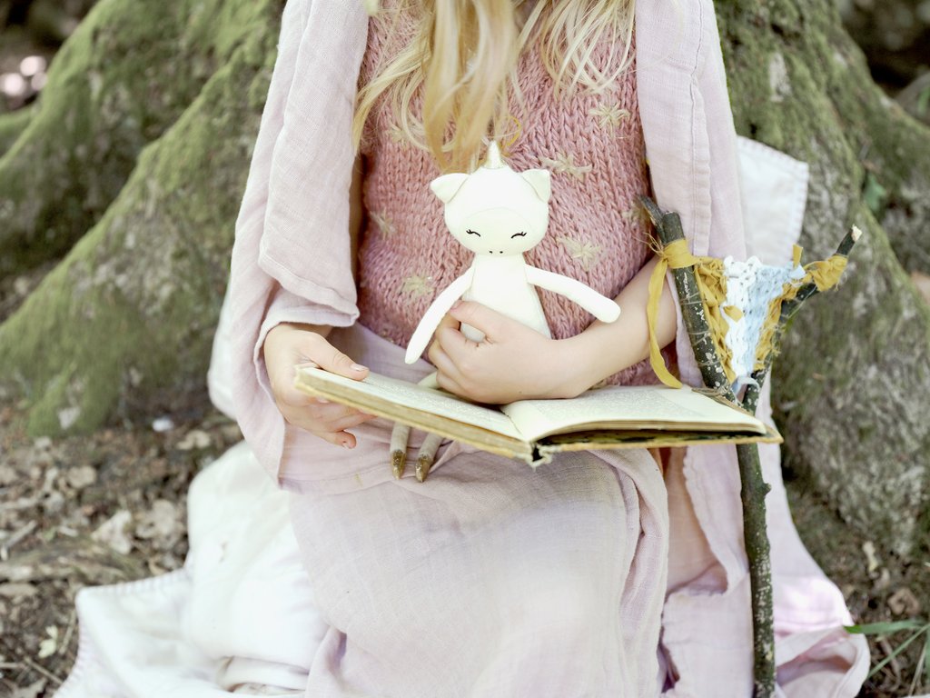 Morbida bambola di stoffa color panna a forma di unicorno in braccio a una bambina