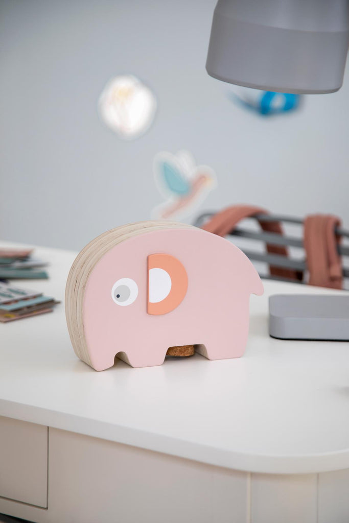 Salvadanaio in legno di colore rosa a forma di elefantino su una scrivania