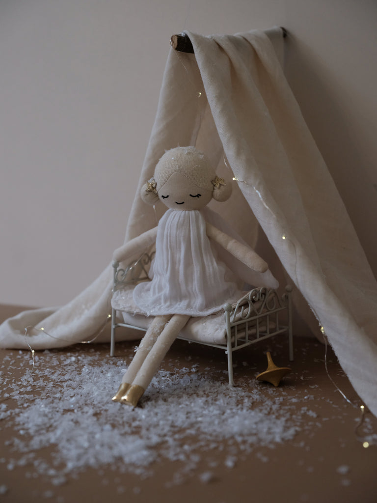 Fata invernale. Bambola in stoffa con vestitino bianco naturale seduta su un lettino