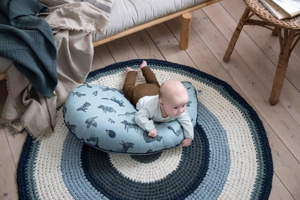 Tappeto rotondo in cotone a anelli concentrici multicolori disposto sul pavimento di una cameretta con sopra un neonato