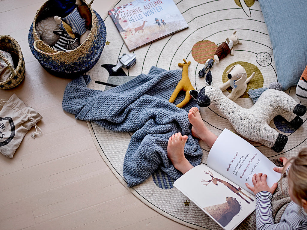 Lama di stoffa in cotone con altri pupazzi e oggetti su un tappeto accanto ad una bambina seduta