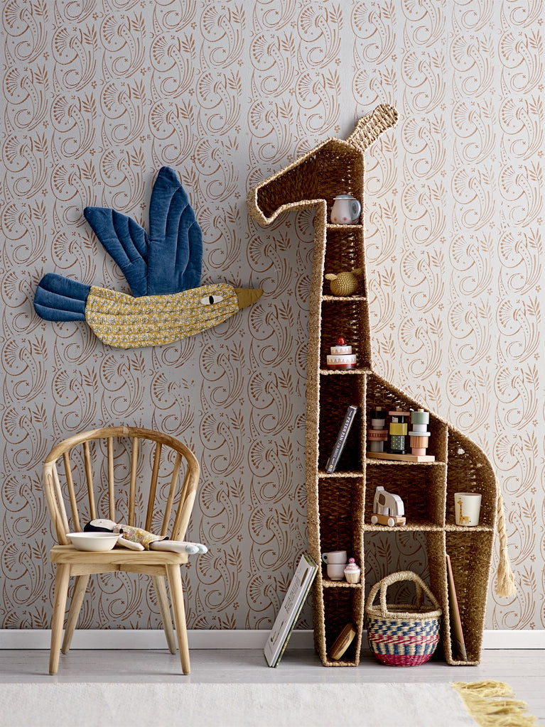 Bambola mora con vestitino floreale su una sedia di vimini accanto una libreria a forma di giraffa con vari oggetti
