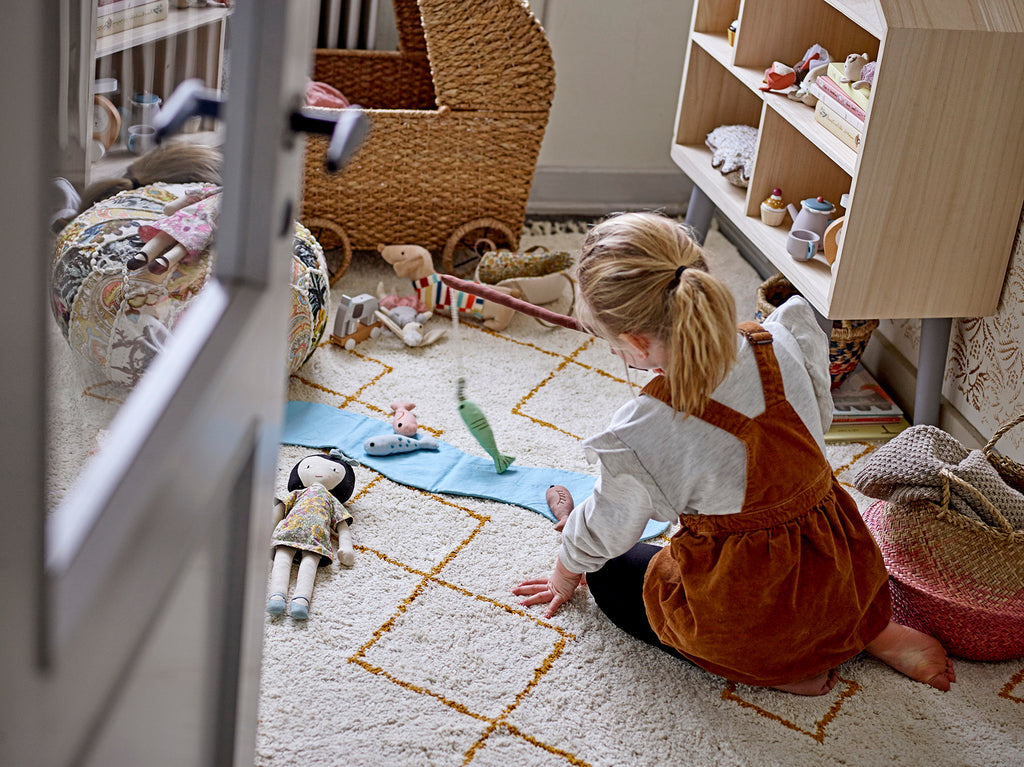 Carrozzina per bambole e pupazzi intrecciata in fibre naturali di bankuan con ruote in una cameretta arredata di fronte ad una bambina che gioca