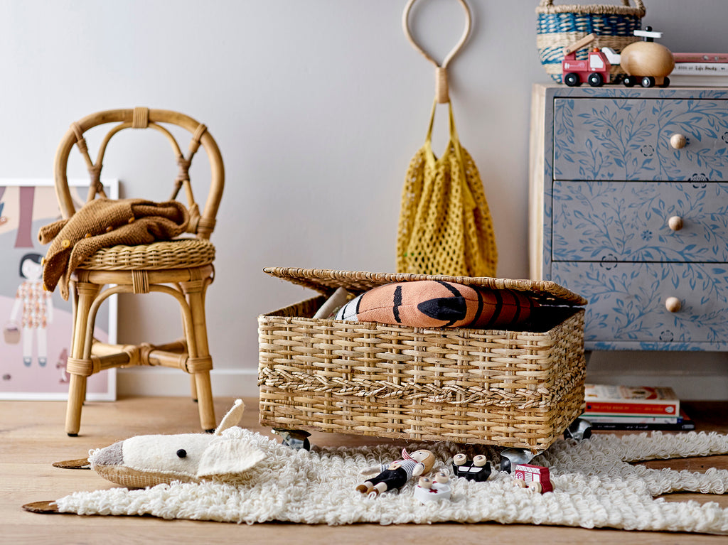 Cameretta arredata con tappeto pecoram sedia e cassettone in vimini e altri oggetti