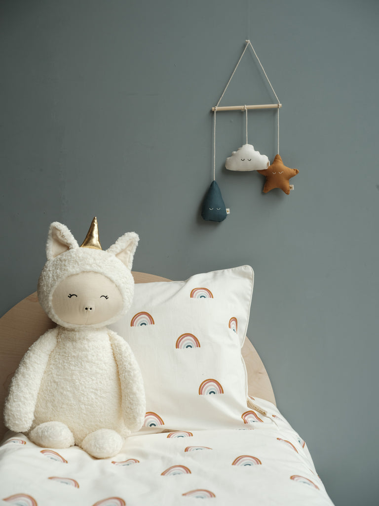 Unicorno peluche alto 54 cm appoggiato ad un cuscino sopra un lettino