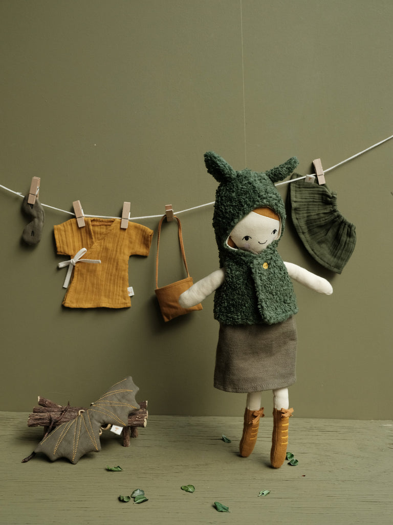 Bambola in cotone davanti a vestiti da bambola appesi ad un filo ad asciugare
