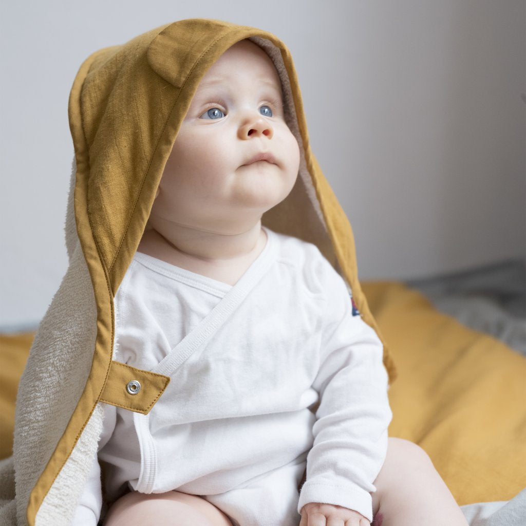 Asciugamano color ocra in cotone per bambini con cappuccio indossato da un neonato
