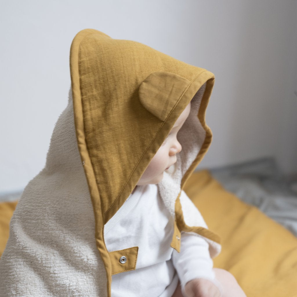 Asciugamano color ocra in cotone per bambini con cappuccio indossato da un neonato