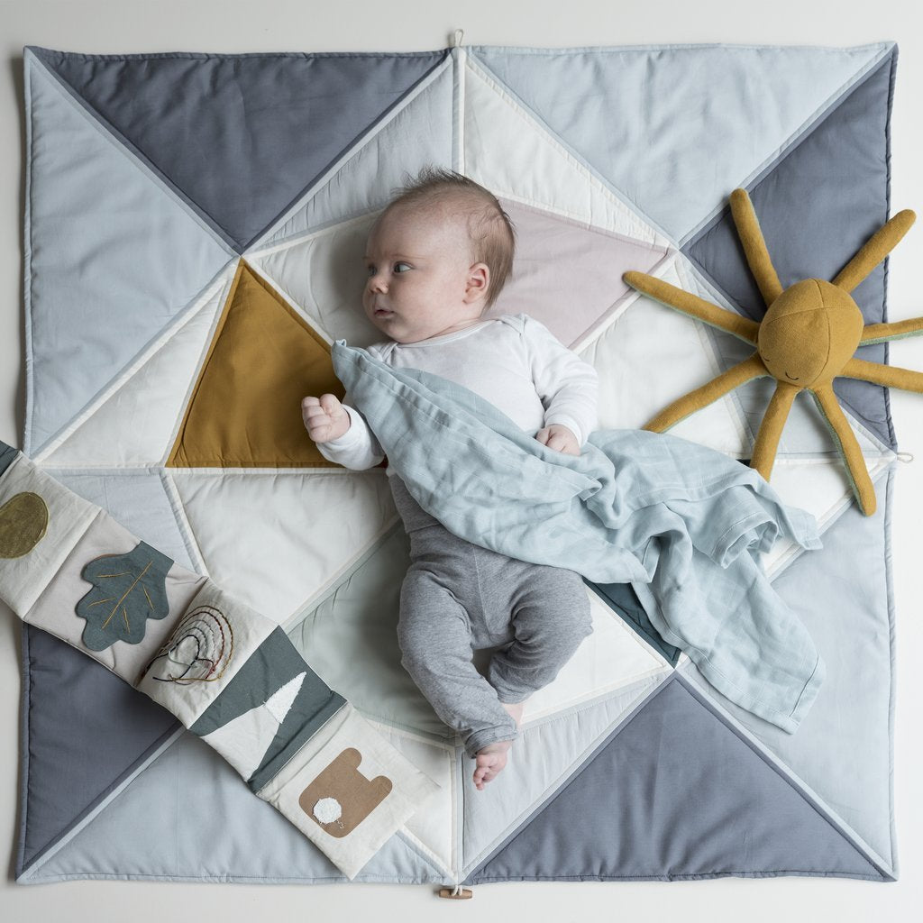Sonaglio in stoffa color ocra a forma di polpo disteso su una copertina accanto ad un neinato addormentato