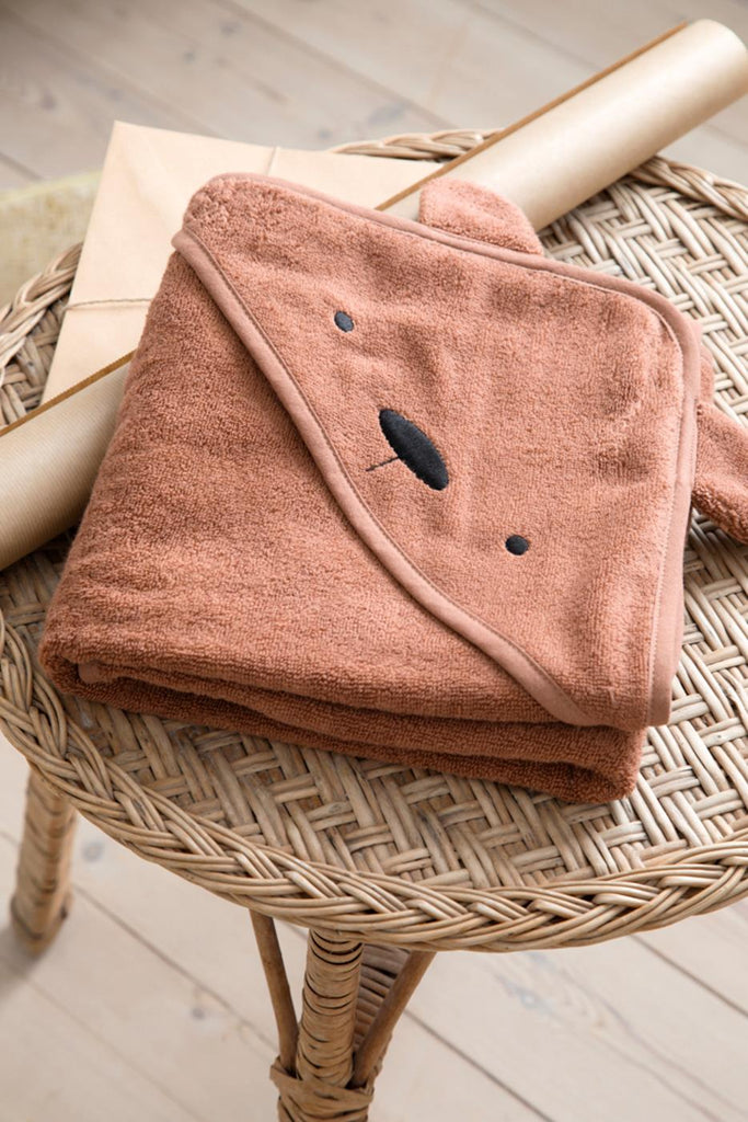 Asciugamano in cotone biologico con cappuccio orso Milo, color marrone. Ripiegato su un tavolino
